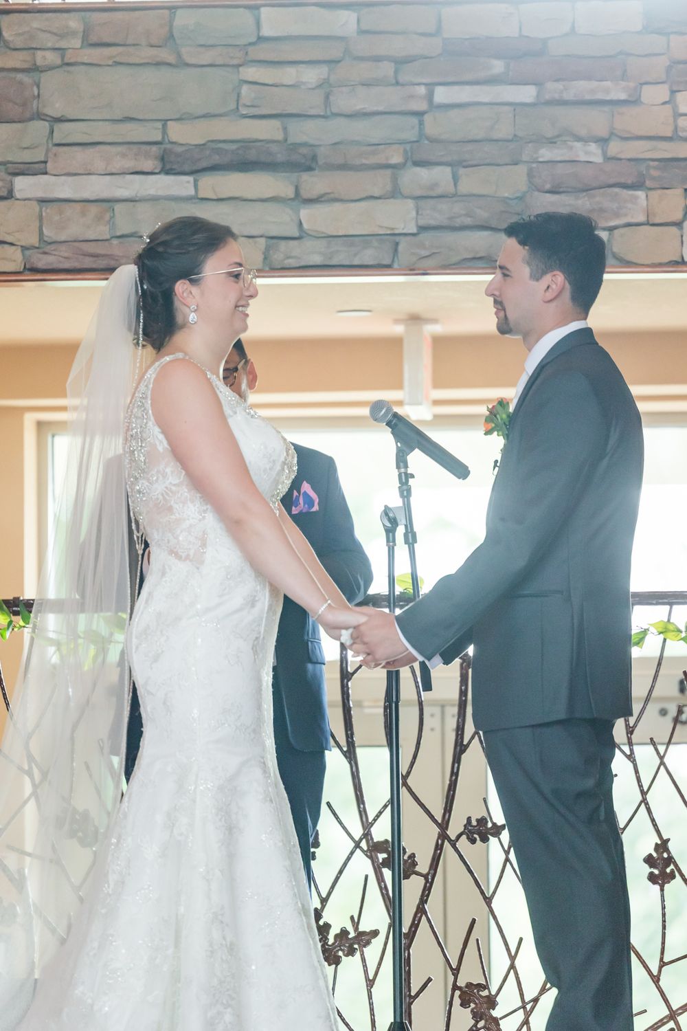 Couple holding hands during their wedding ceremony with microphone stand between them.