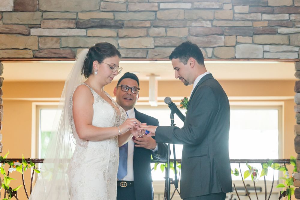 A wedding ceremony in progress with a couple exchanging rings in front of a stone wall backdrop.