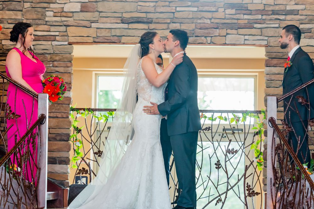 Wedding ceremony kiss with pink-dressed attendant and guests watching from the sides.