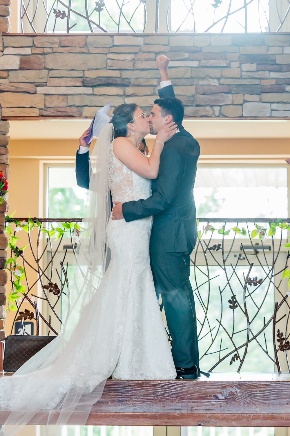 A celebratory wedding kiss moment with the couple raising their arms in joy.