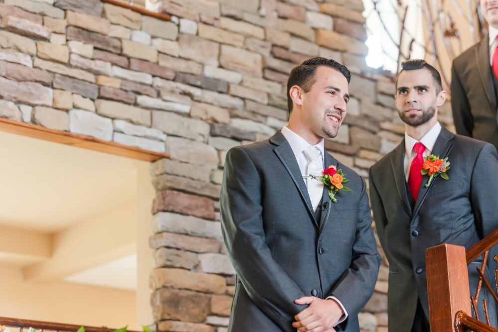 Two men in formal suits with boutonnieres stand at wedding altar with stone backdrop.