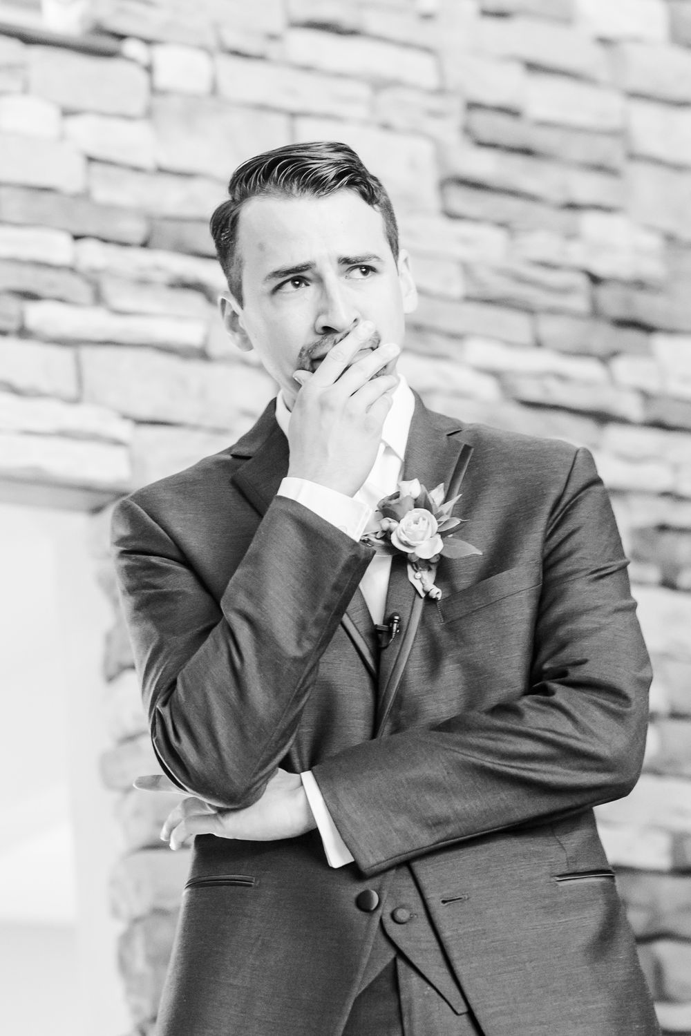 Black and white portrait of groom showing emotional expression against stone wall.
