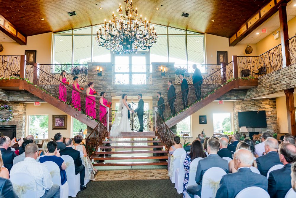 Wedding ceremony in progress with bridal party on grand staircase and guests seated below.