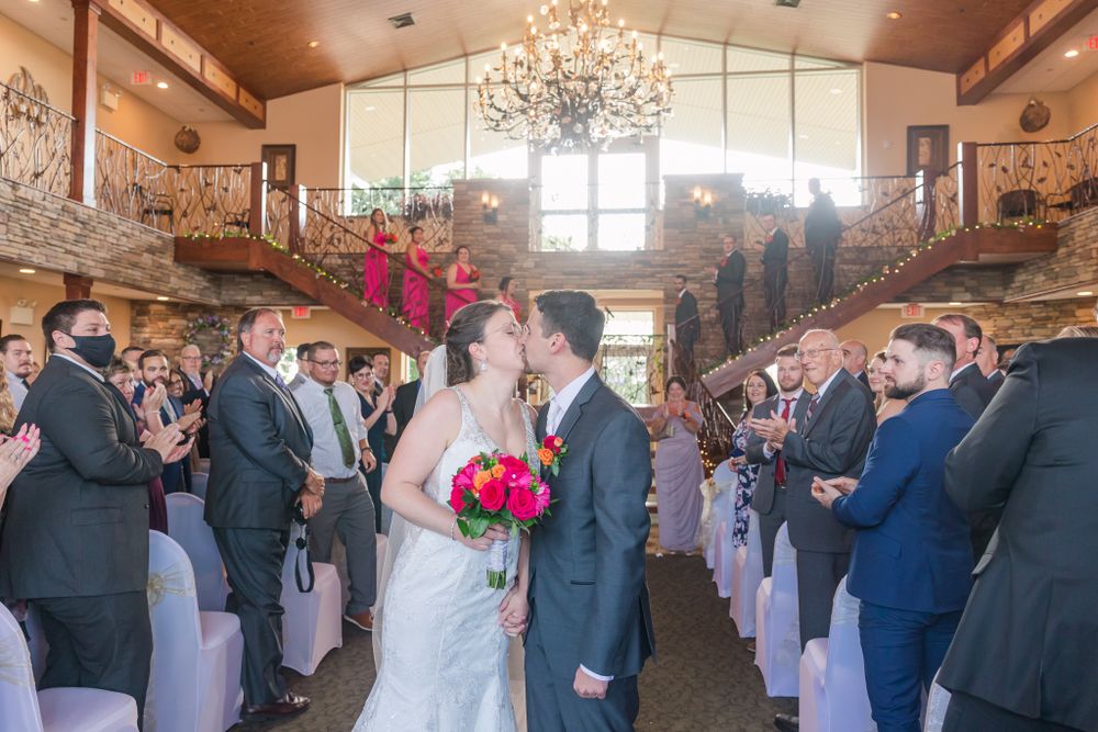 Wedding couple sharing moment surrounded by guests in elegant venue with chandelier.