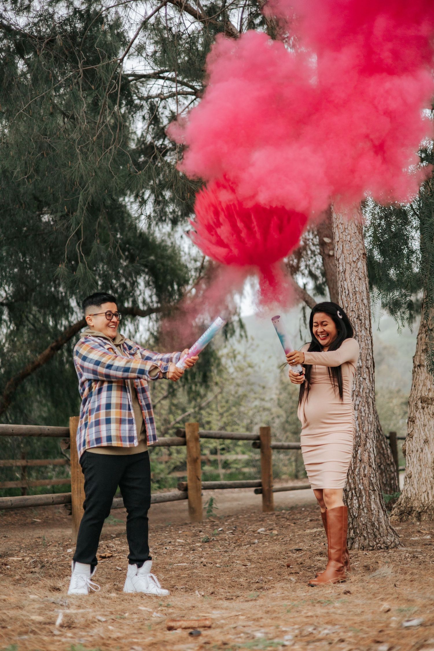 A couple celebrates with red smoke bombs in an outdoor forest setting.