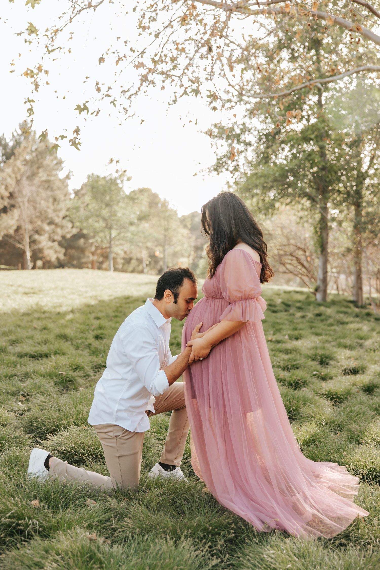 A romantic proposal moment in a sun-dappled meadow with a flowing pink dress.