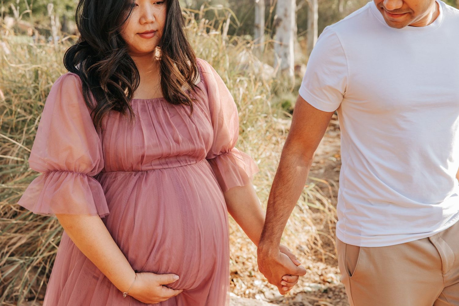 A couple holds hands outdoors while wearing coordinated casual outfits during a maternity photoshoot.