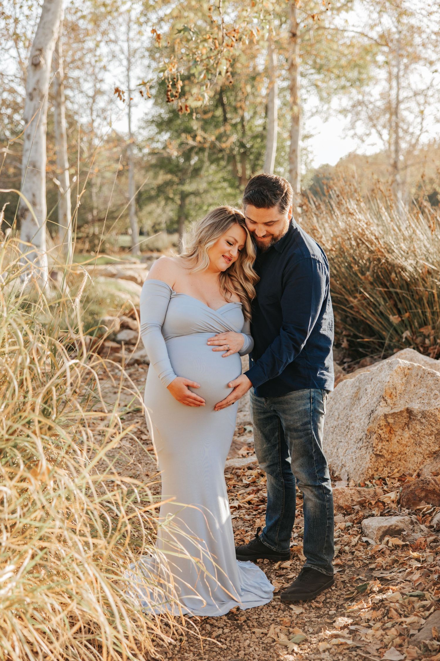 An intimate maternity portrait in a natural setting with tall grass and trees.