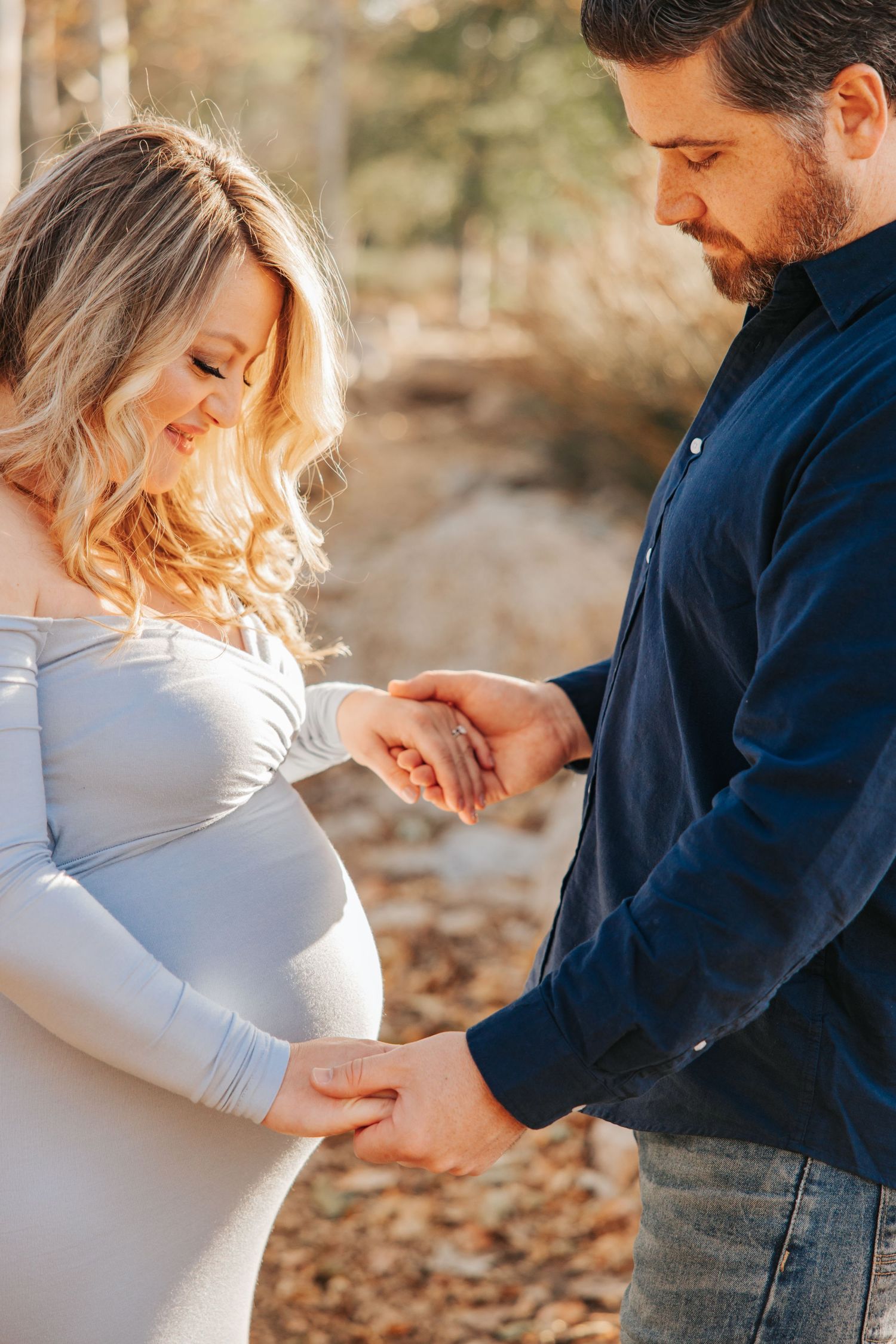 An intimate maternity moment captured in warm sunlight among autumn trees.