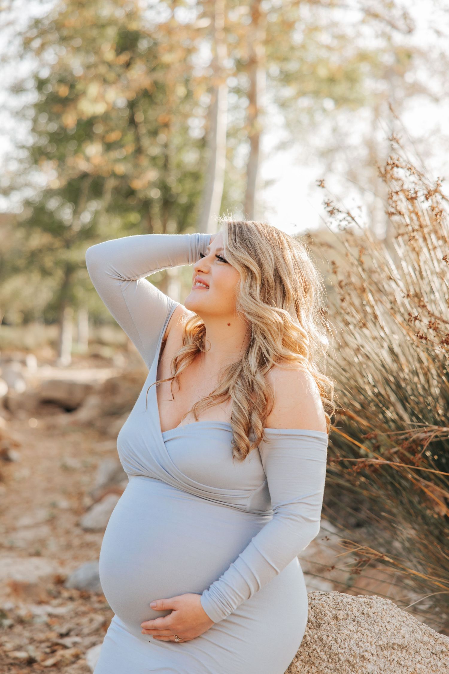 A radiant maternity portrait of an expectant mother in a light blue dress outdoors.