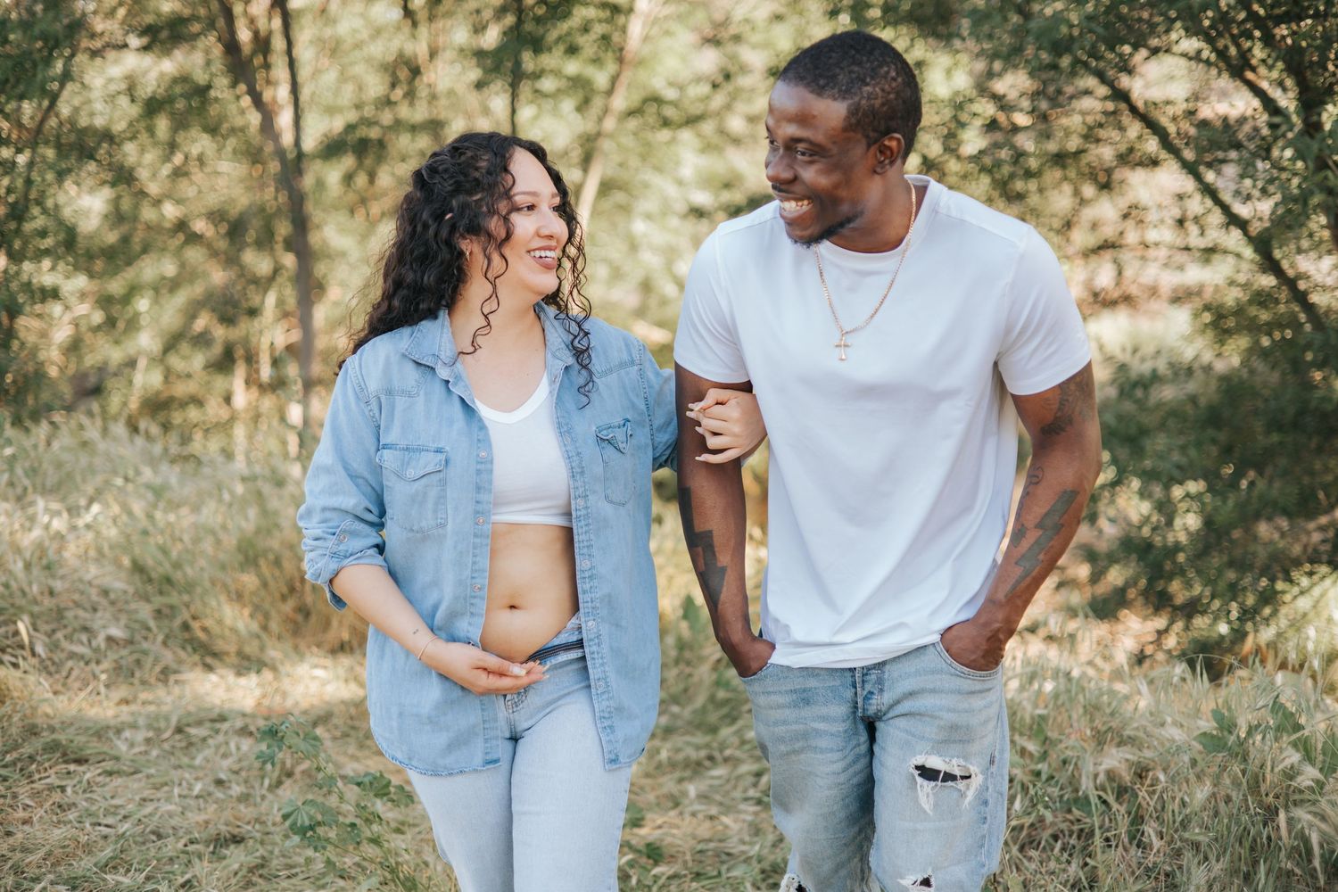 Couple sharing a laugh during outdoor maternity photography session in casual attire.