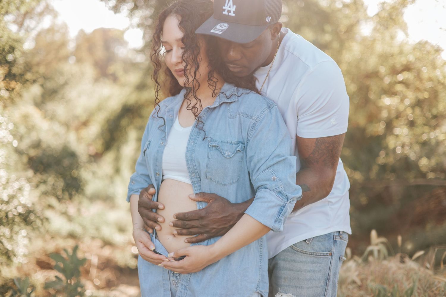 Couple embracing during maternity photoshoot outdoors in casual denim outfits.