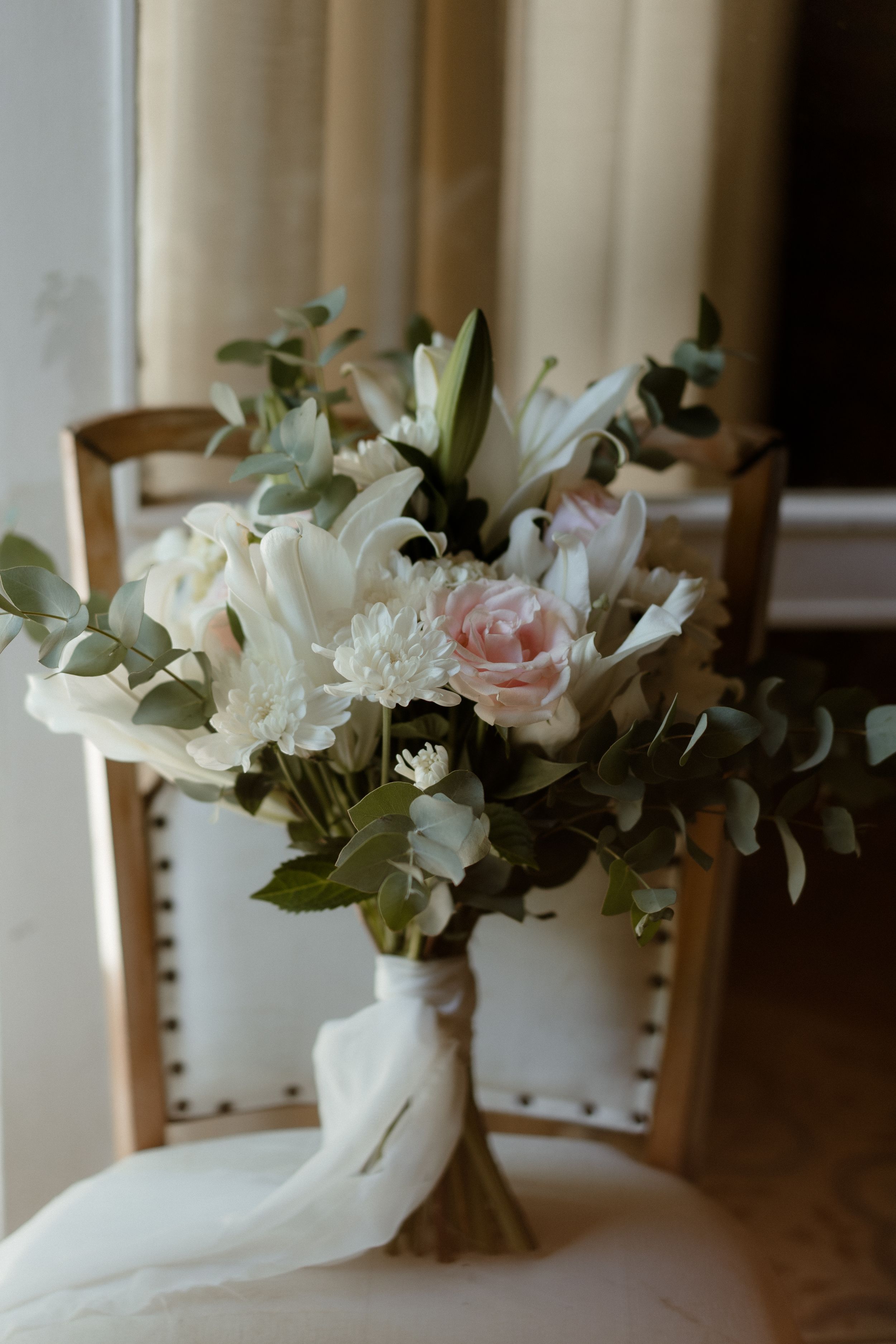 Elegant floral arrangement with white lilies and pale pink roses in natural light.