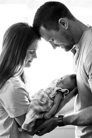 Black and white portrait of a couple lovingly holding their newborn baby in an intimate moment.