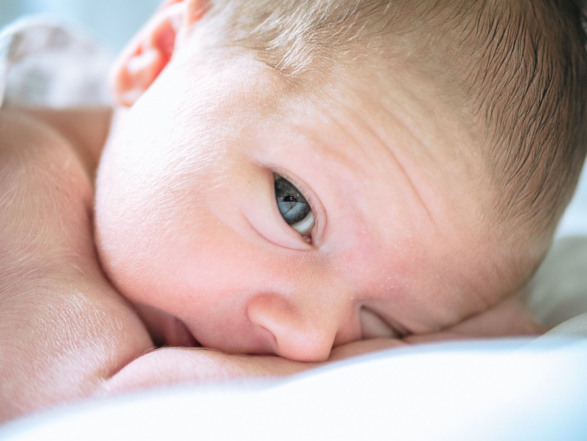 Close-up view of an infant resting on soft white bedding.