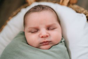Sleeping infant wrapped in mint green swaddle rests peacefully in basket.