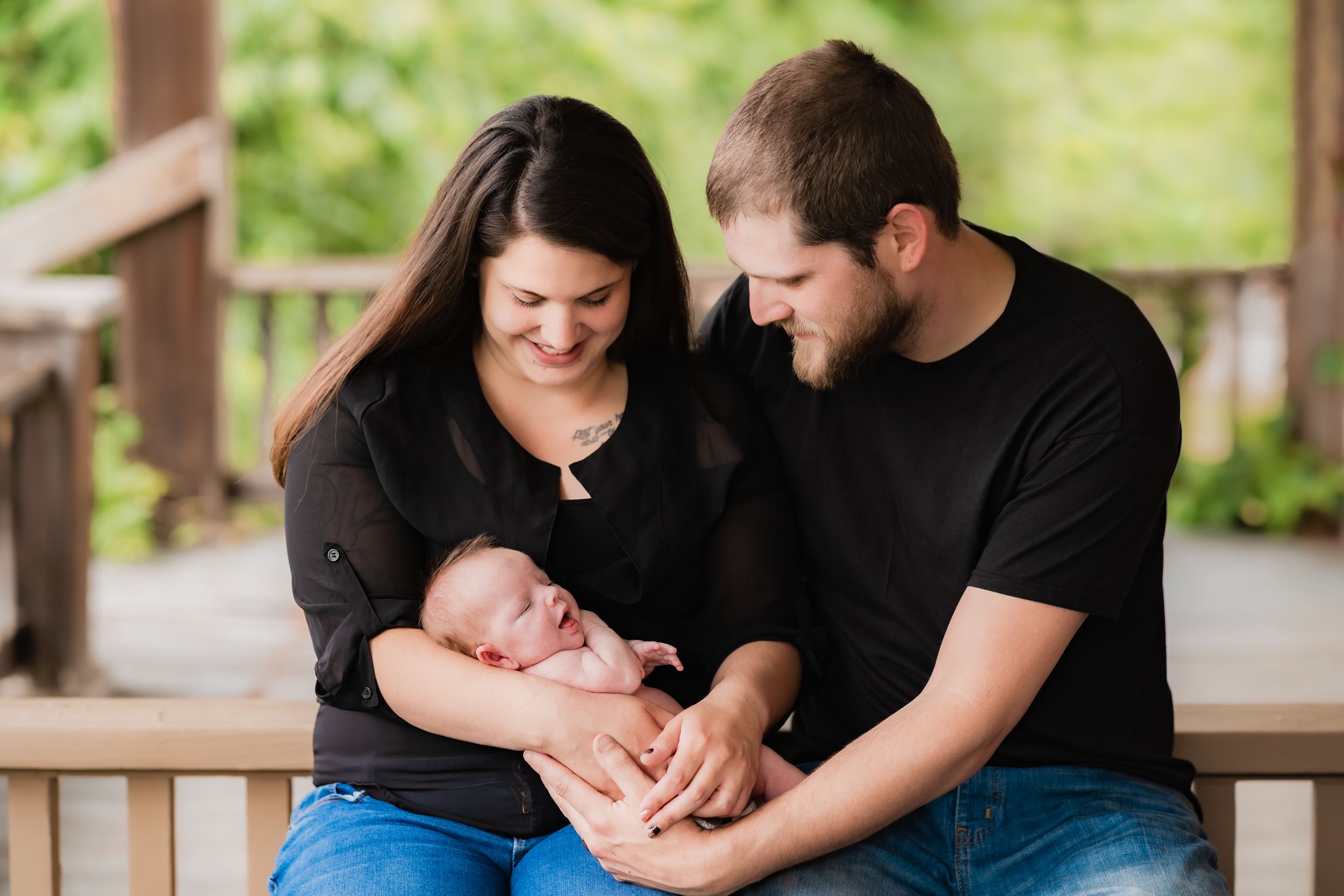 Parents on wooden porch sharing tender moment with their newborn.