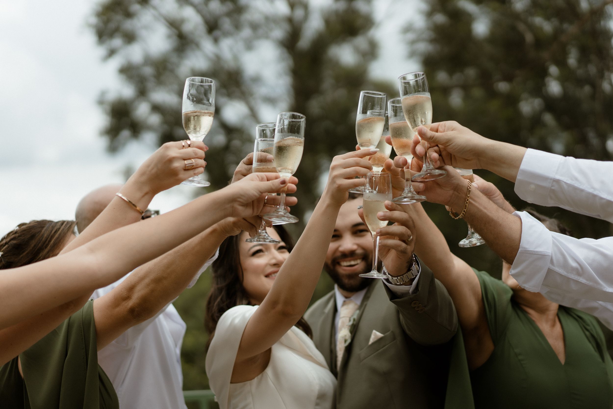 Wedding party raises champagne glasses in celebratory toast outdoors.