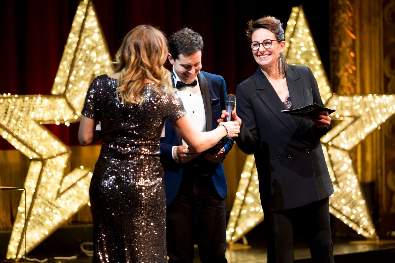 A celebratory awards ceremony moment in front of a large illuminated star backdrop.
