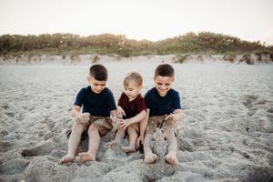 Three young boys sitting together on sandy beach dunes at sunset.