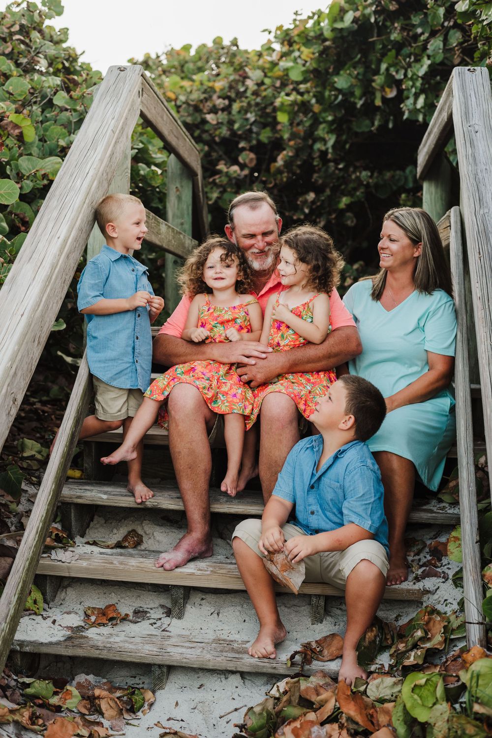 A family shares a candid moment together on wooden beach stairs surrounded by greenery.