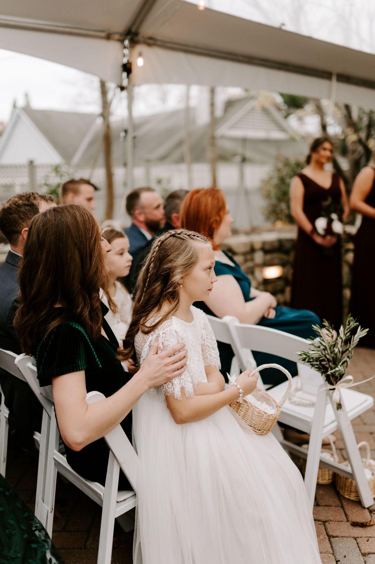 Young flower girls in white dresses at wedding ceremony under tent.