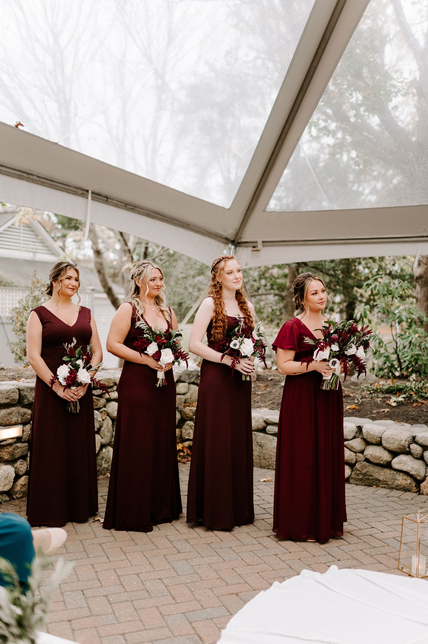 Bridesmaids in burgundy dresses lined up during outdoor wedding ceremony.