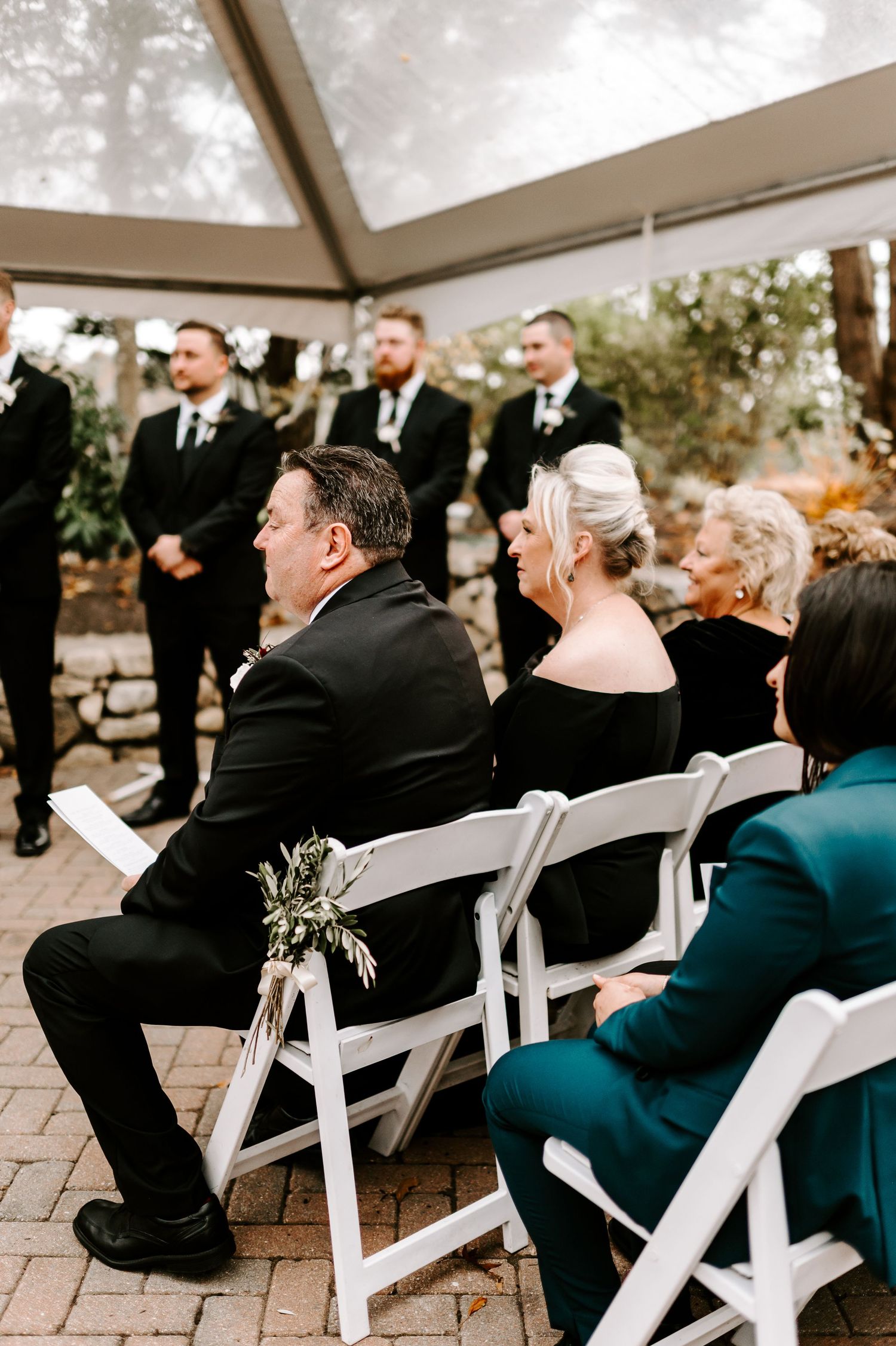 Wedding guests seated in white chairs during outdoor tent ceremony.