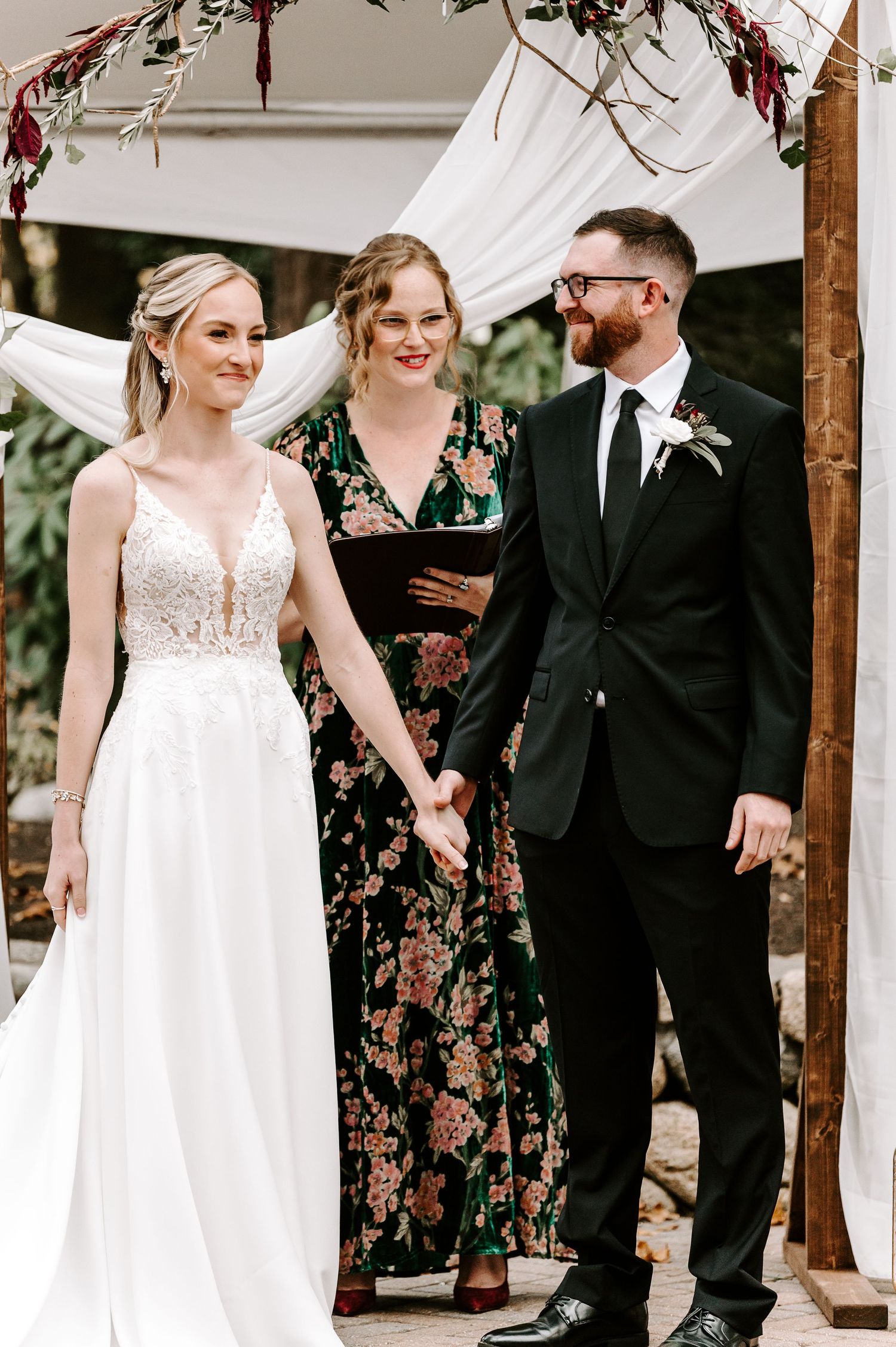 Wedding party in floral dresses and formal attire walking together under wooden pergola.