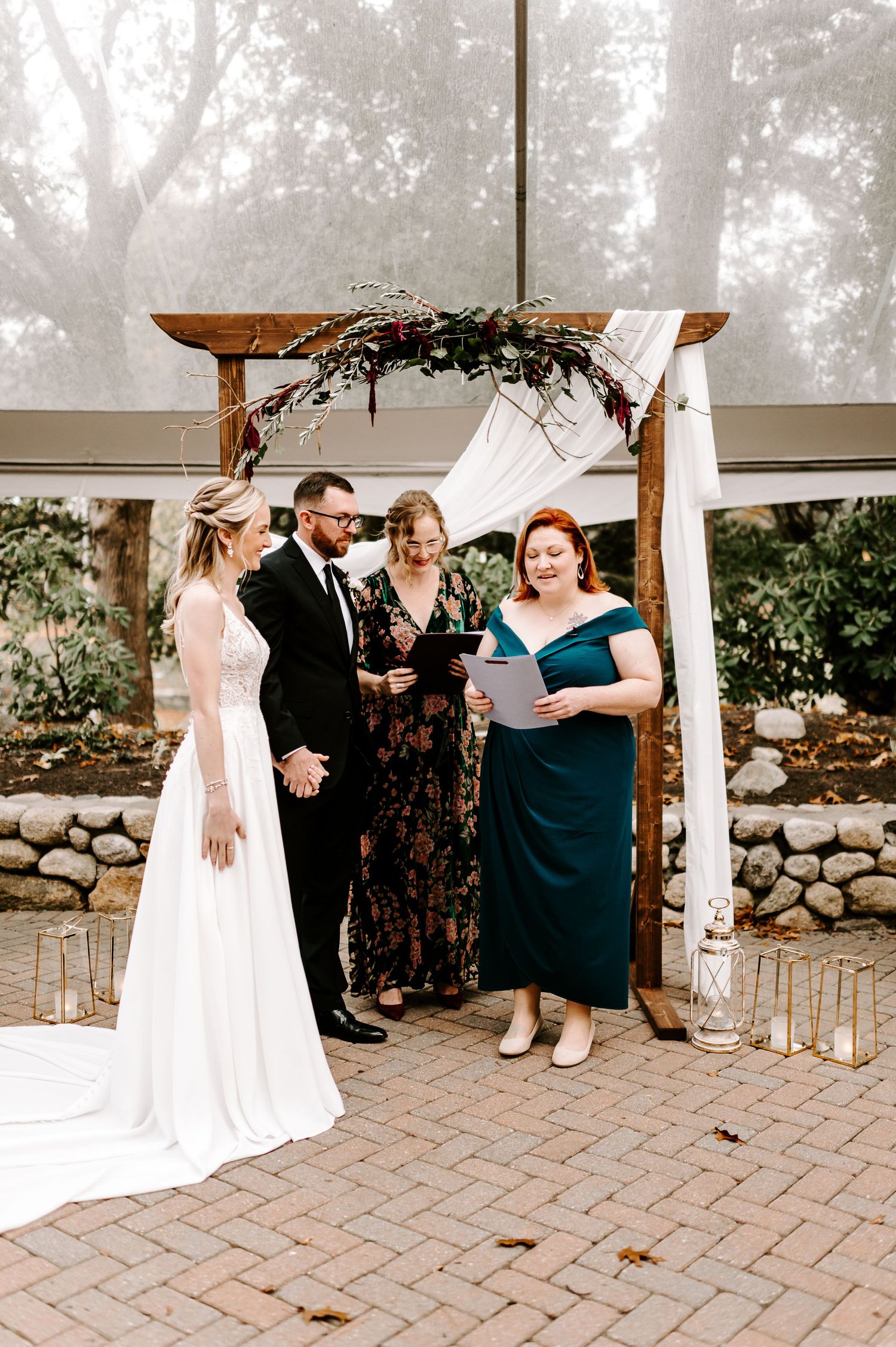 Wedding guests mingle during ceremony under tent with stone wall backdrop.