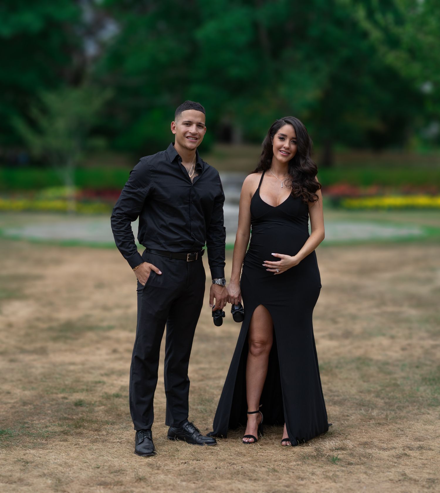 Couple in formal black attire posing together in an outdoor field setting.