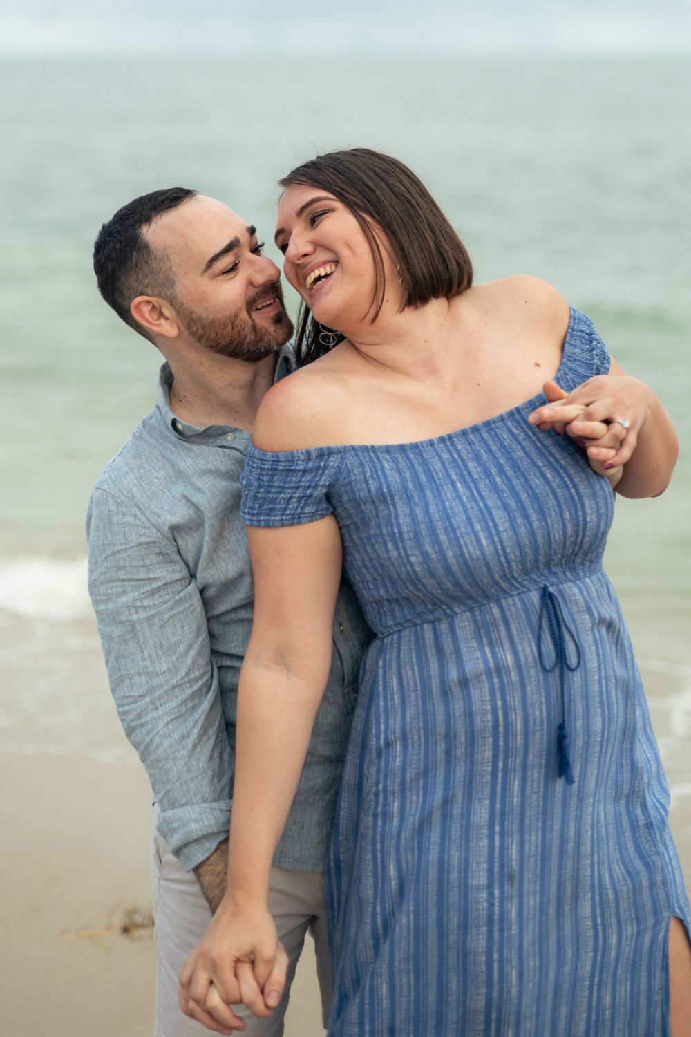 A couple embraces lovingly on the beach, with one wearing a striped blue dress.