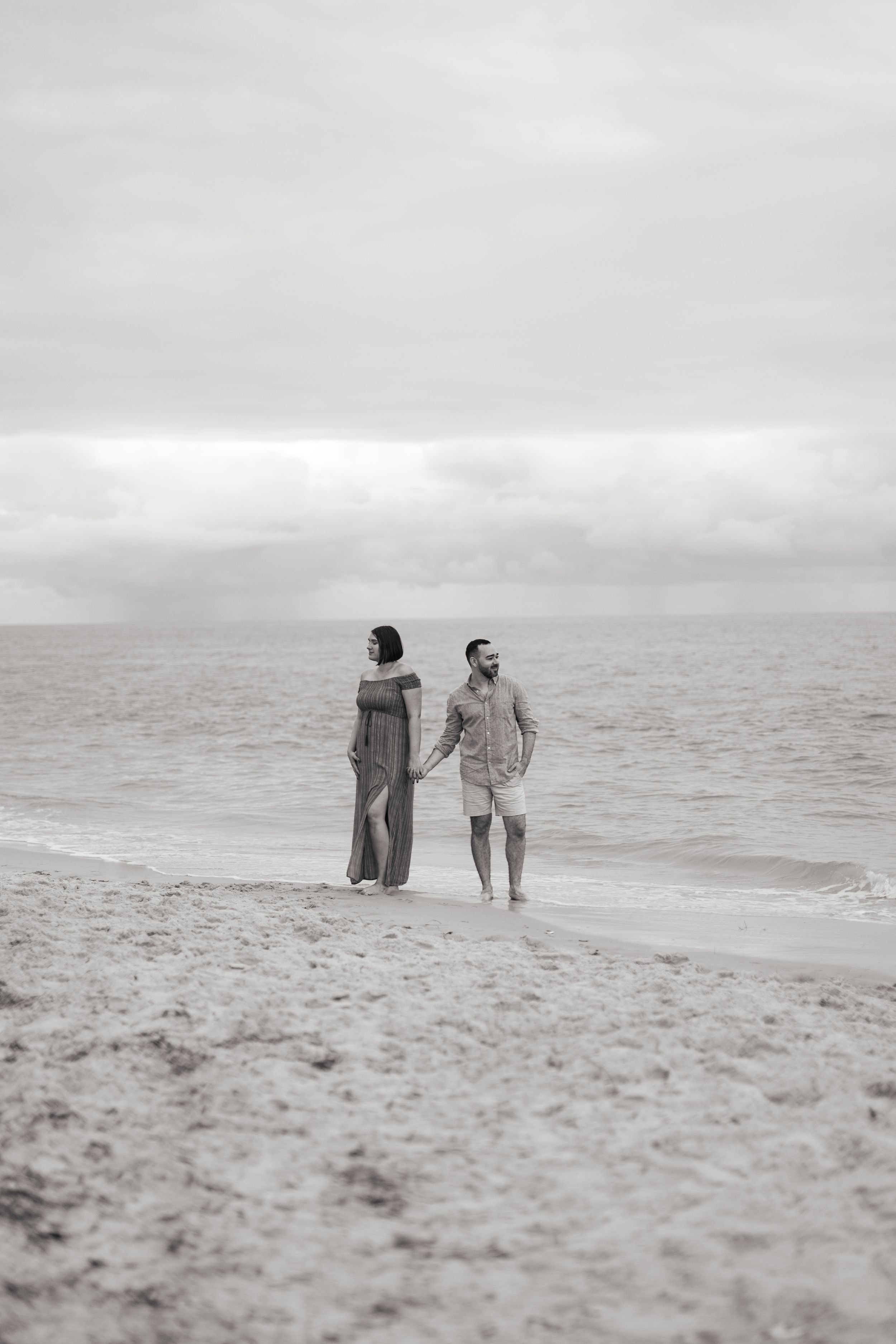 A black and white beach photo captures two figures walking along the misty shoreline.
