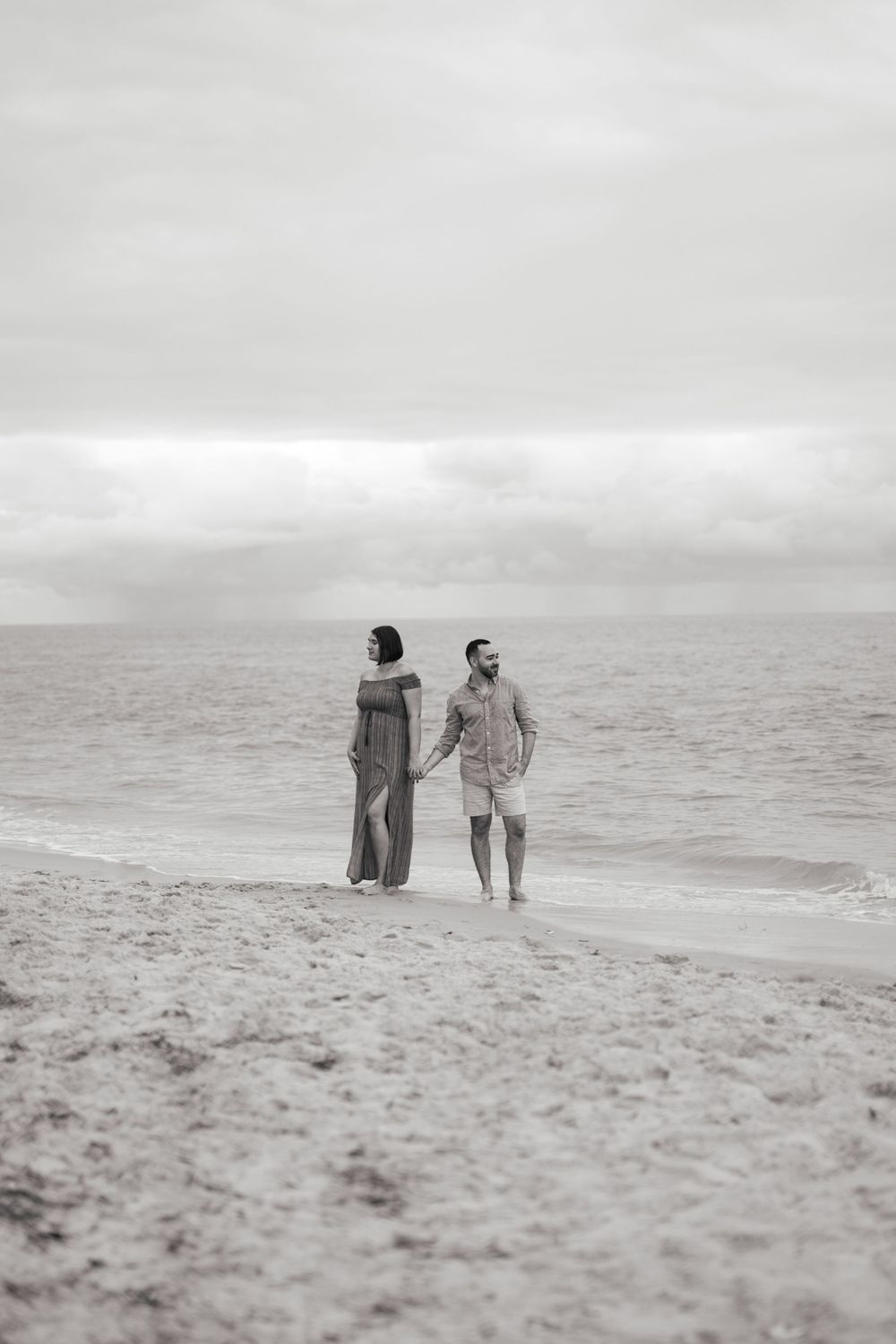 A black and white beach photo captures two figures walking along the misty shoreline.