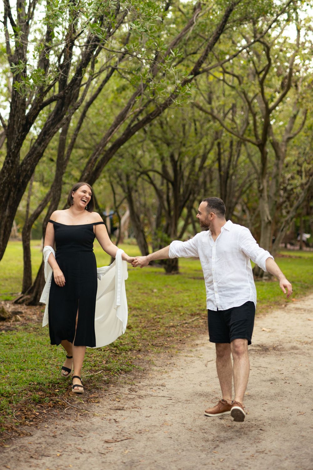 Couple playfully poses for engagement photos on a tree-lined path.