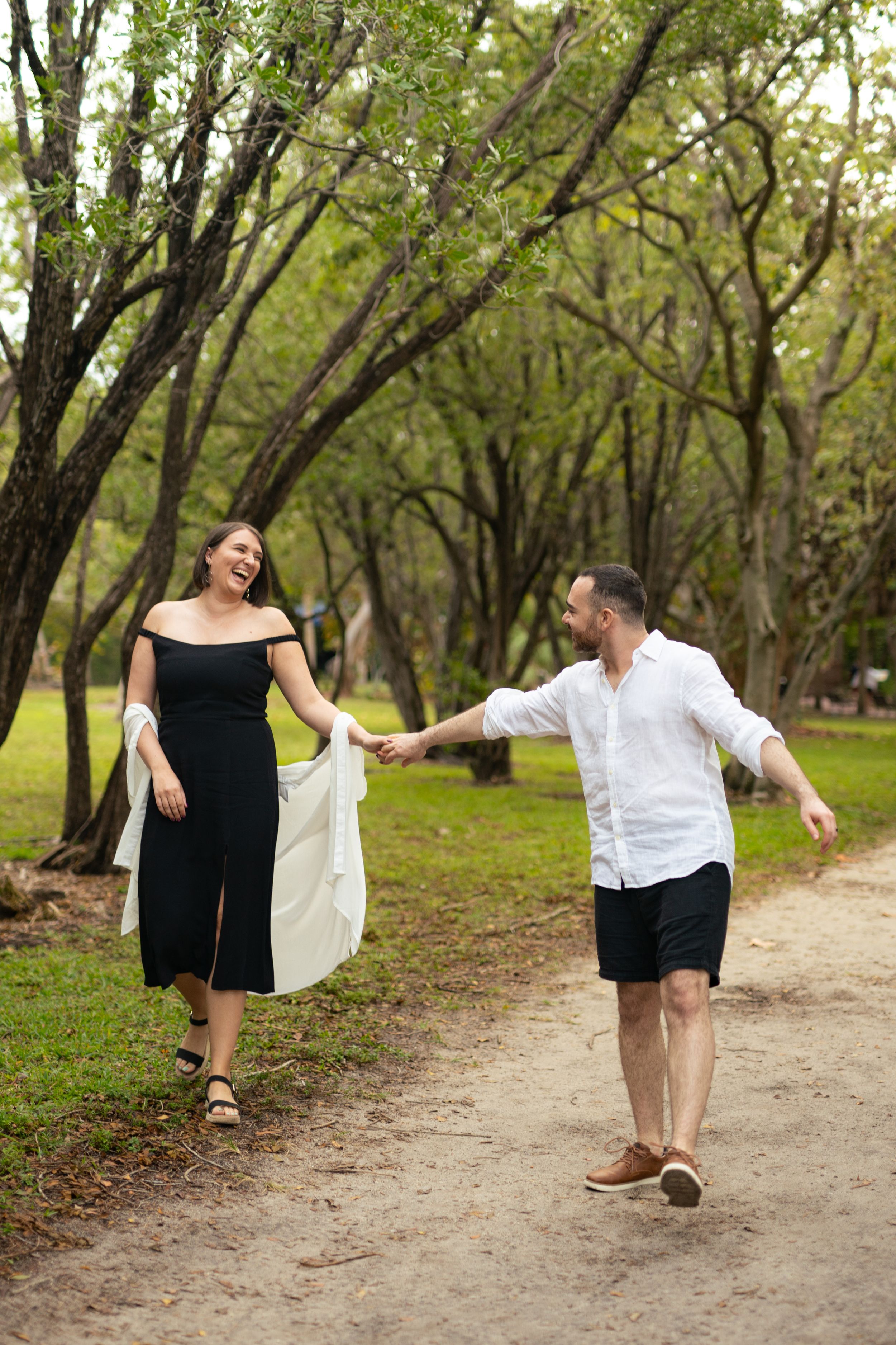 Couple playfully poses for engagement photos on a tree-lined path.