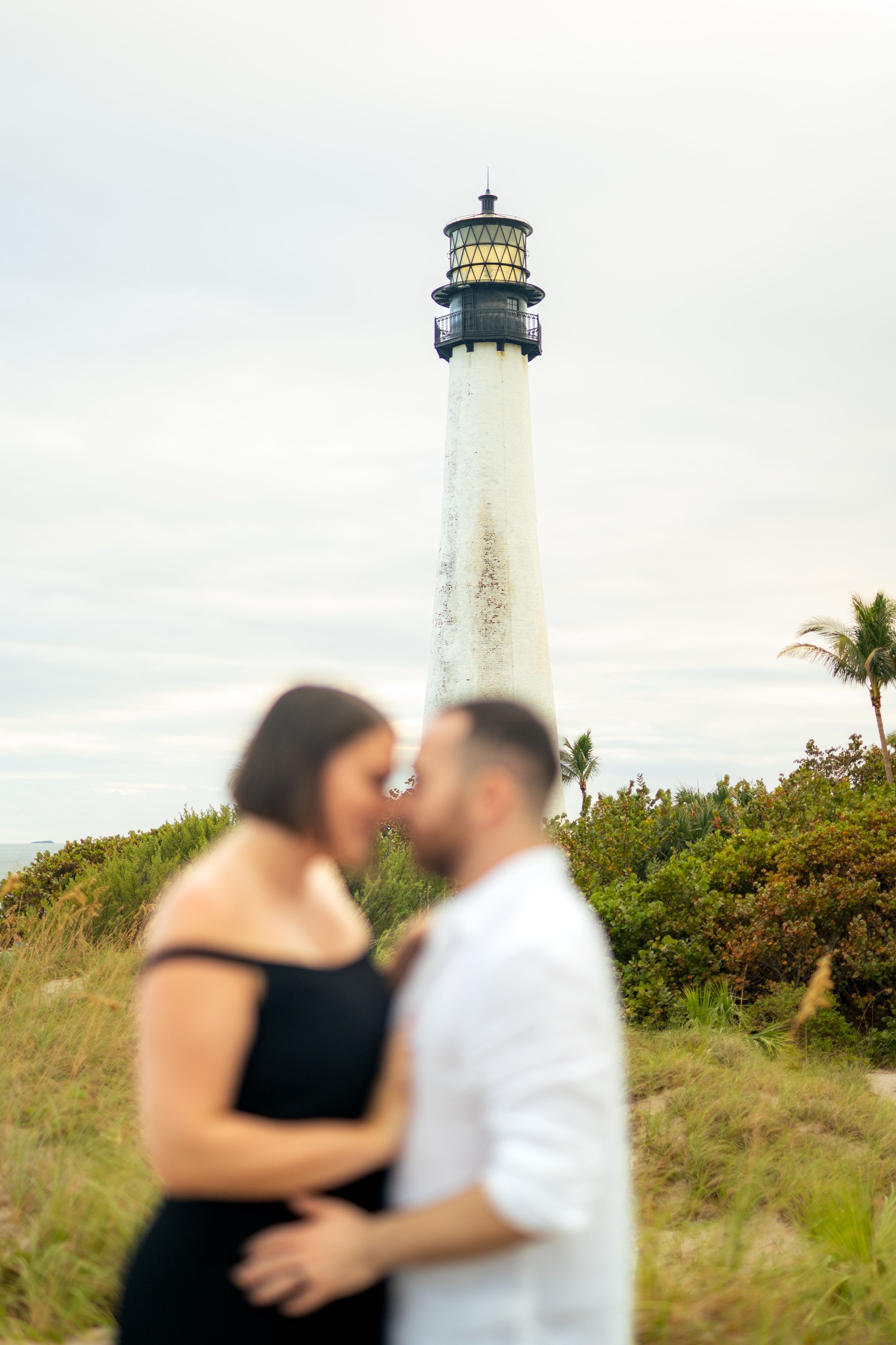 Lighthouse stands tall as couple shares intimate moment on grassy hill.