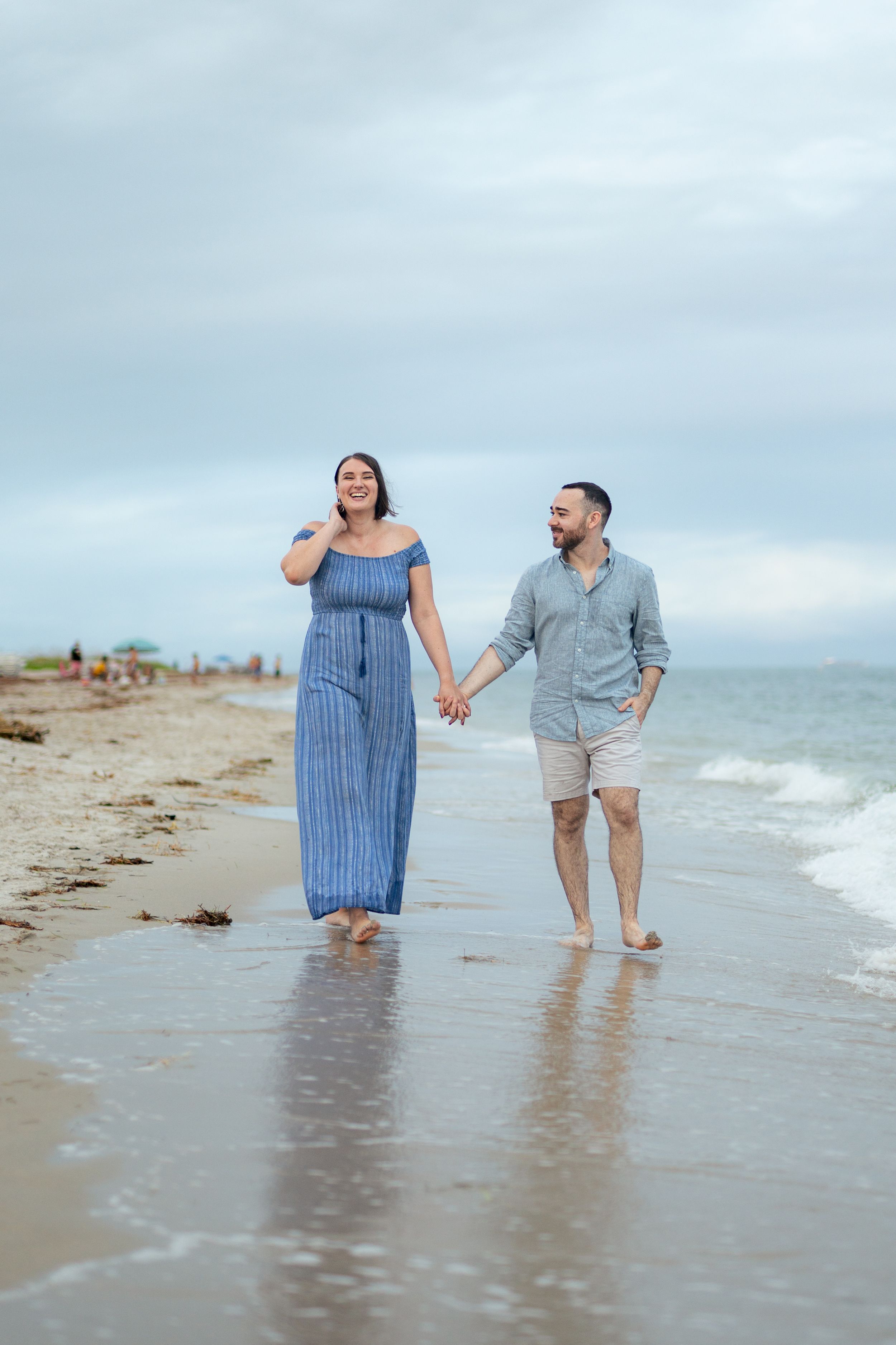 A couple takes a romantic stroll along the water's edge on an overcast beach day.