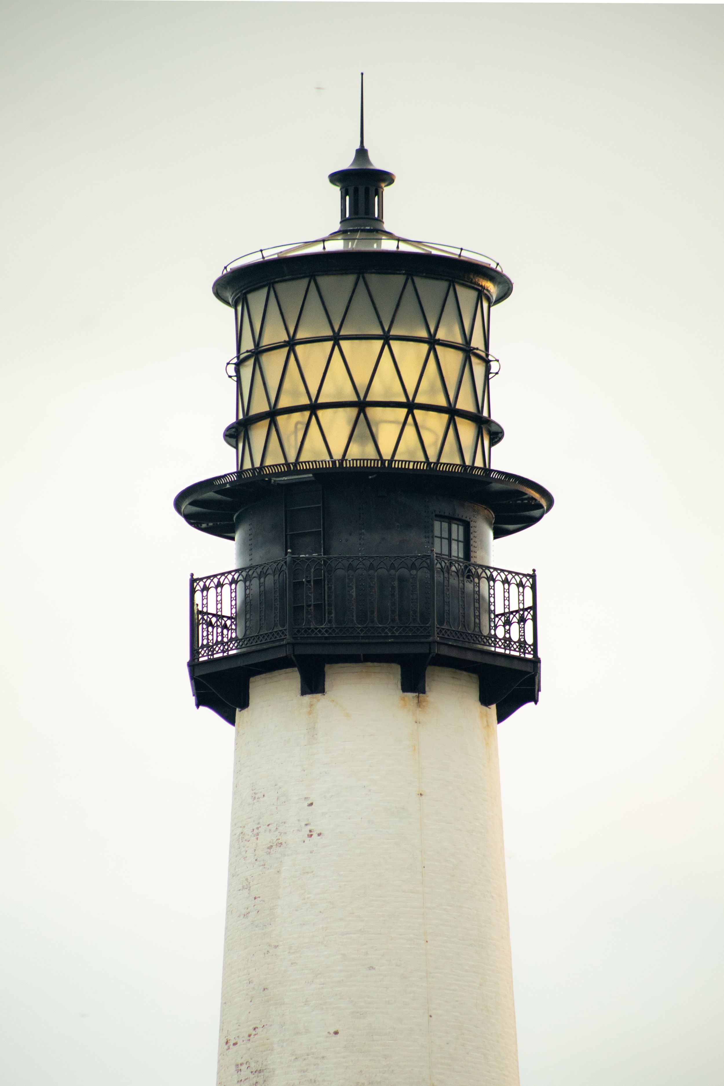 Sequence of white lighthouse tower top with black trim against pale sky.