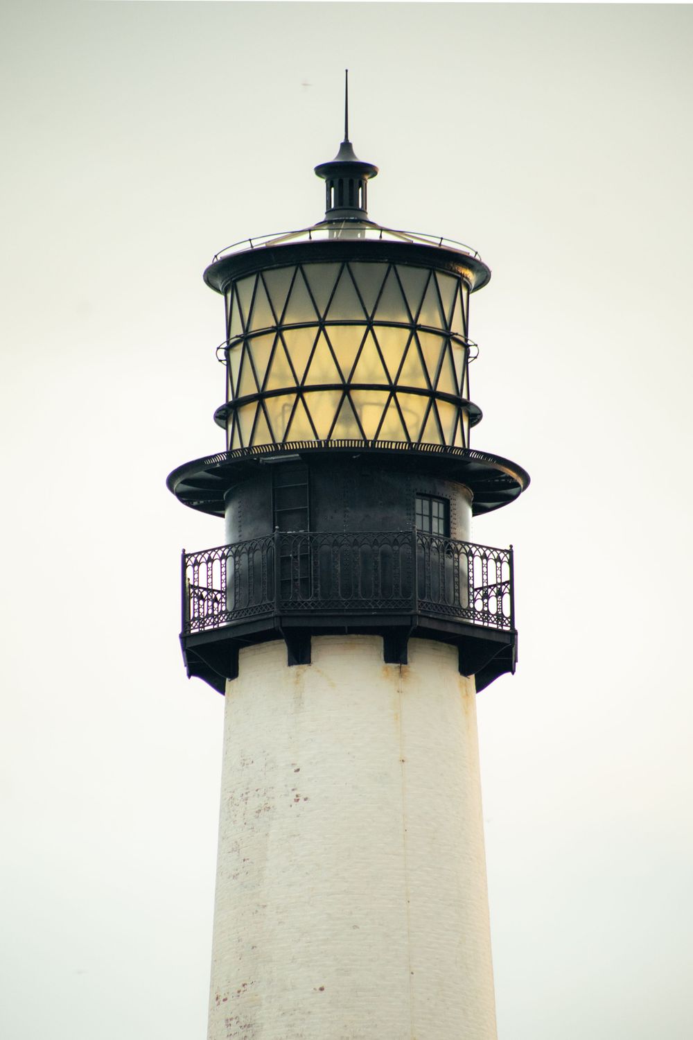 Sequence of white lighthouse tower top with black trim against pale sky.
