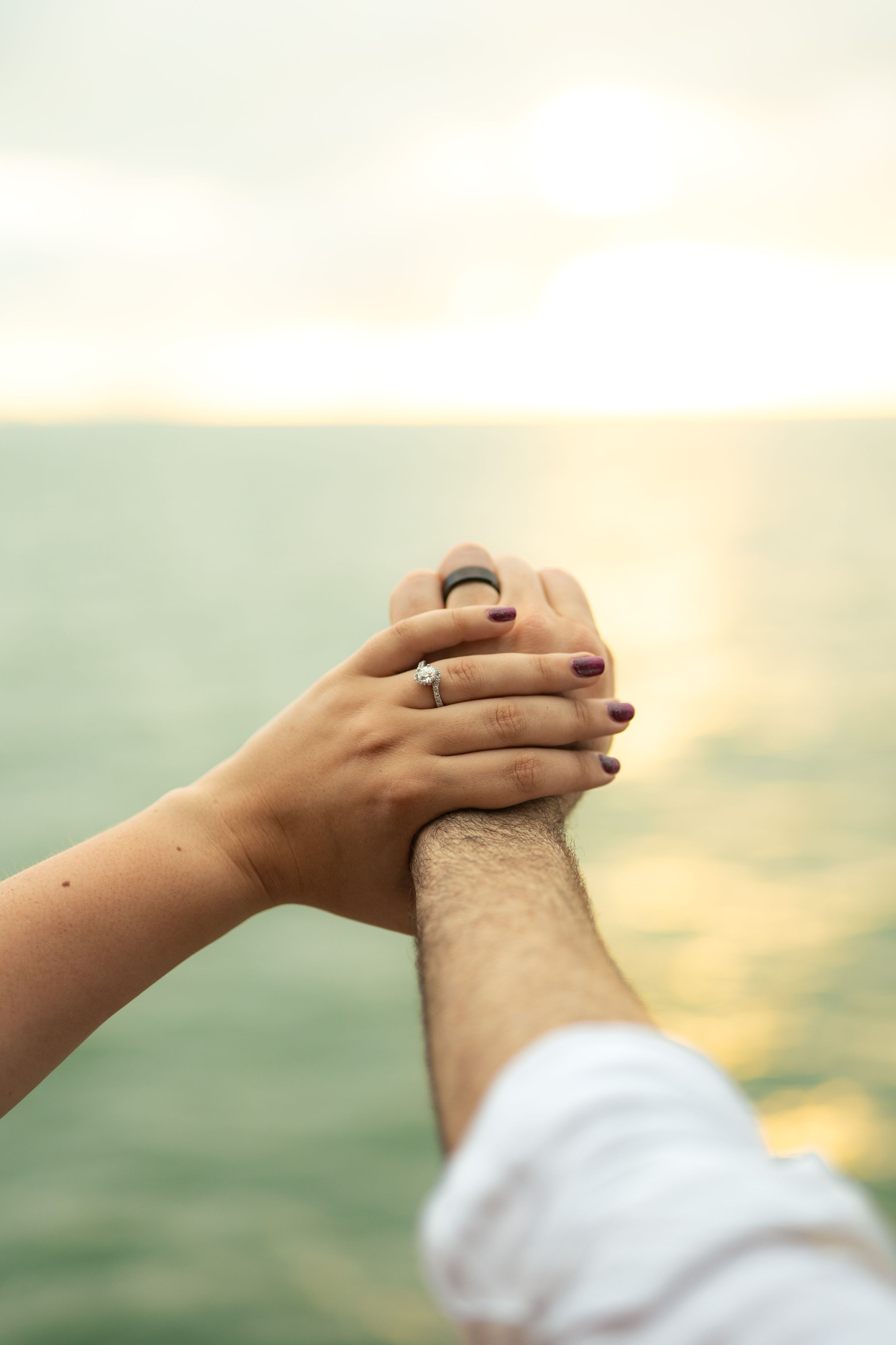 Hands with rings intertwine against a soft, natural background during an intimate moment.