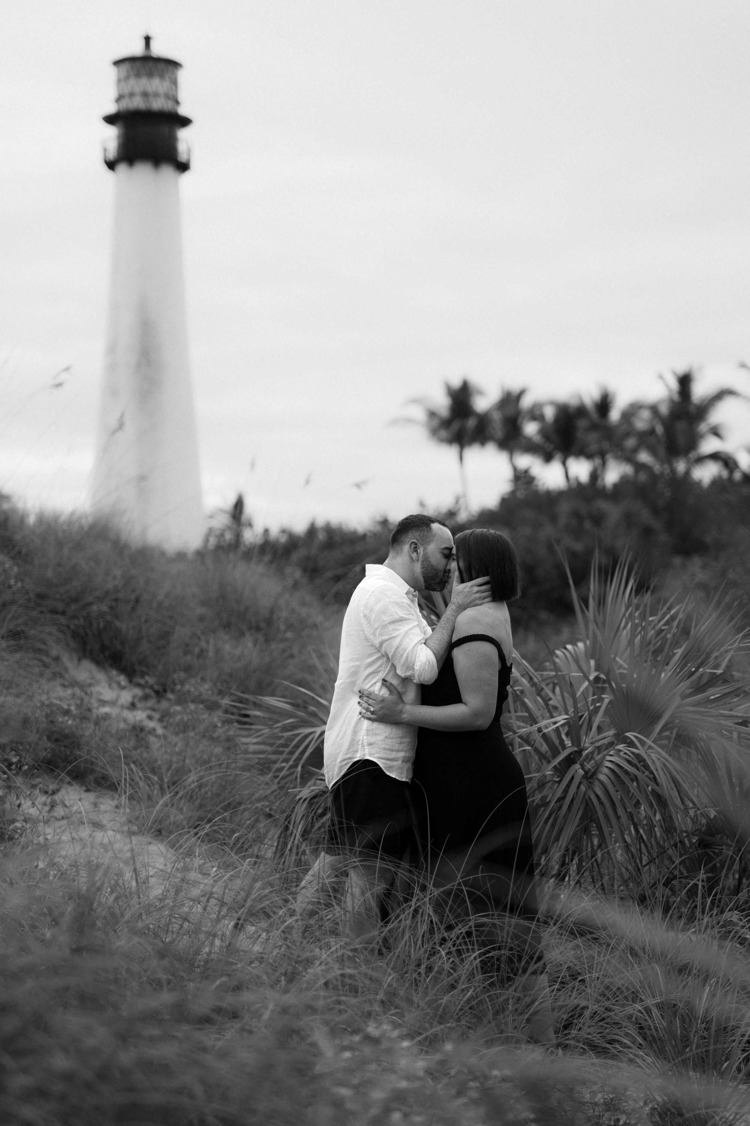 A lighthouse stands tall in the background while a romantic moment unfolds in the grassy foreground.