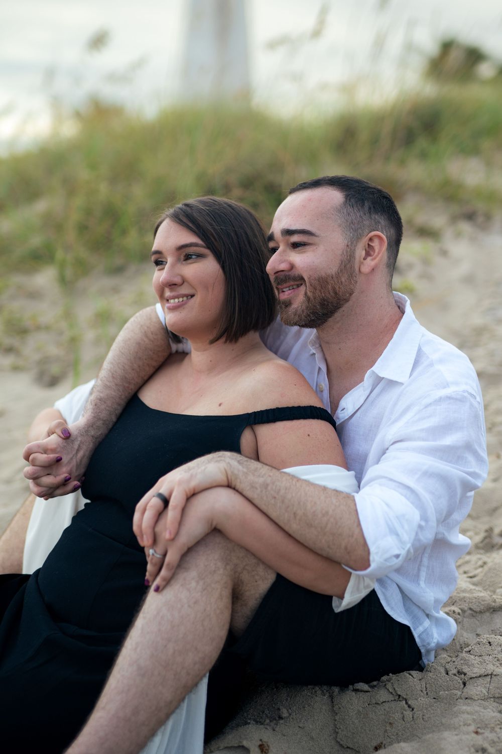 Romantic couple in black and white clothing sits together on sandy beach.
