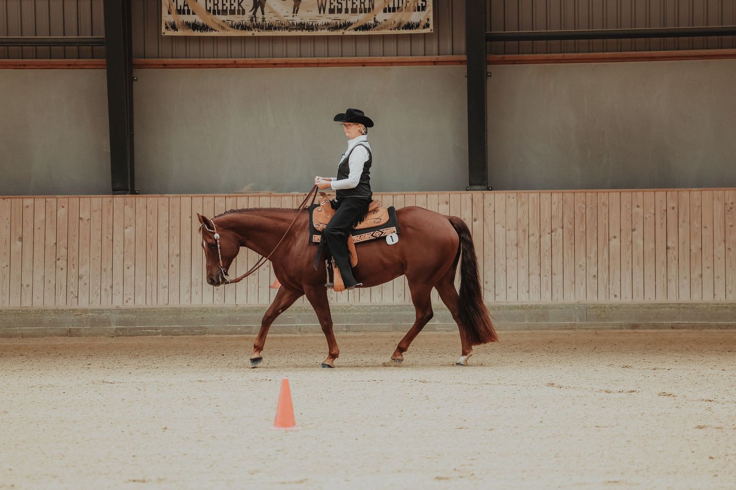 Western horseback riding instruction in an indoor arena with training cones.