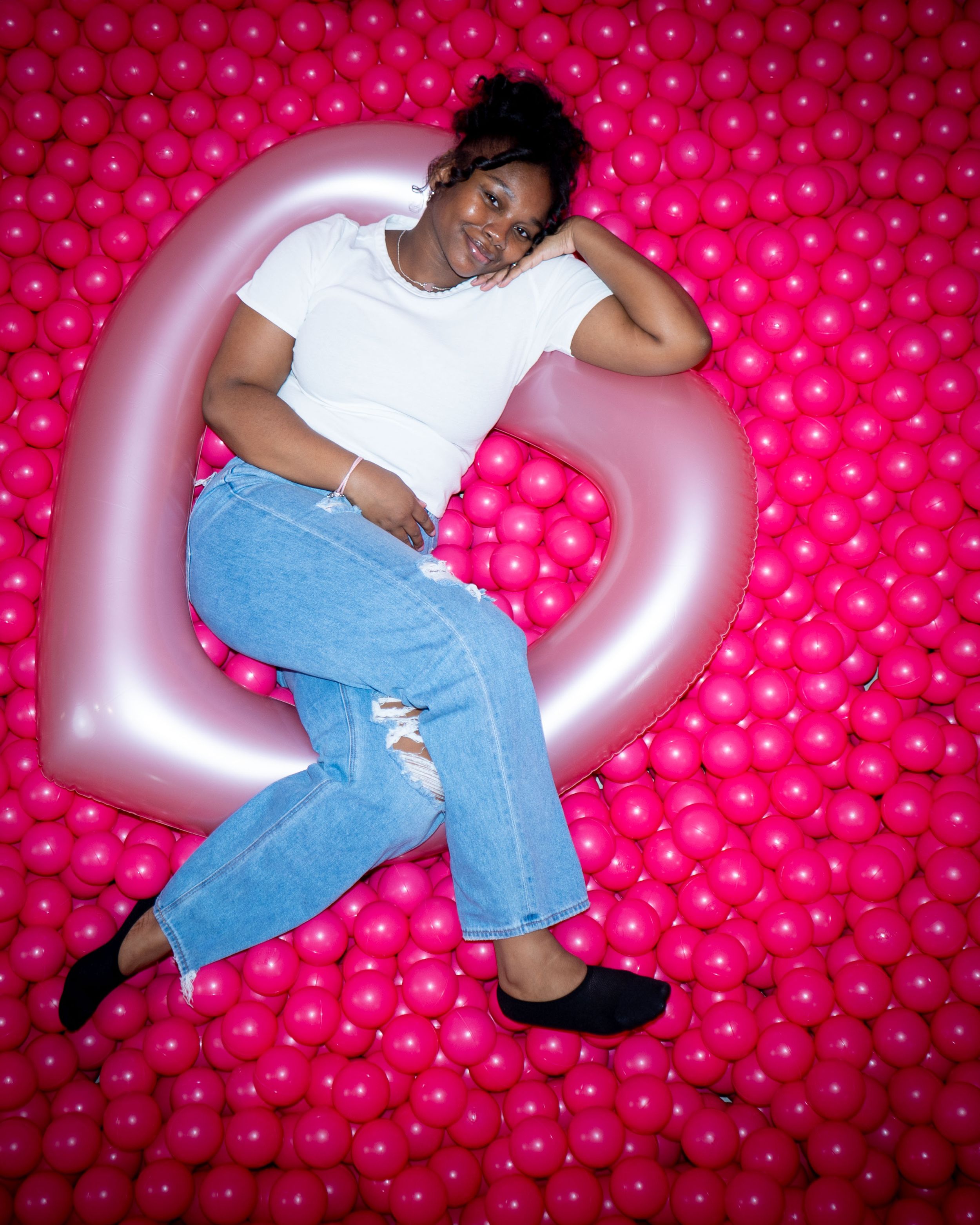 Person lounging on silver inflatable against pink polka dot backdrop.