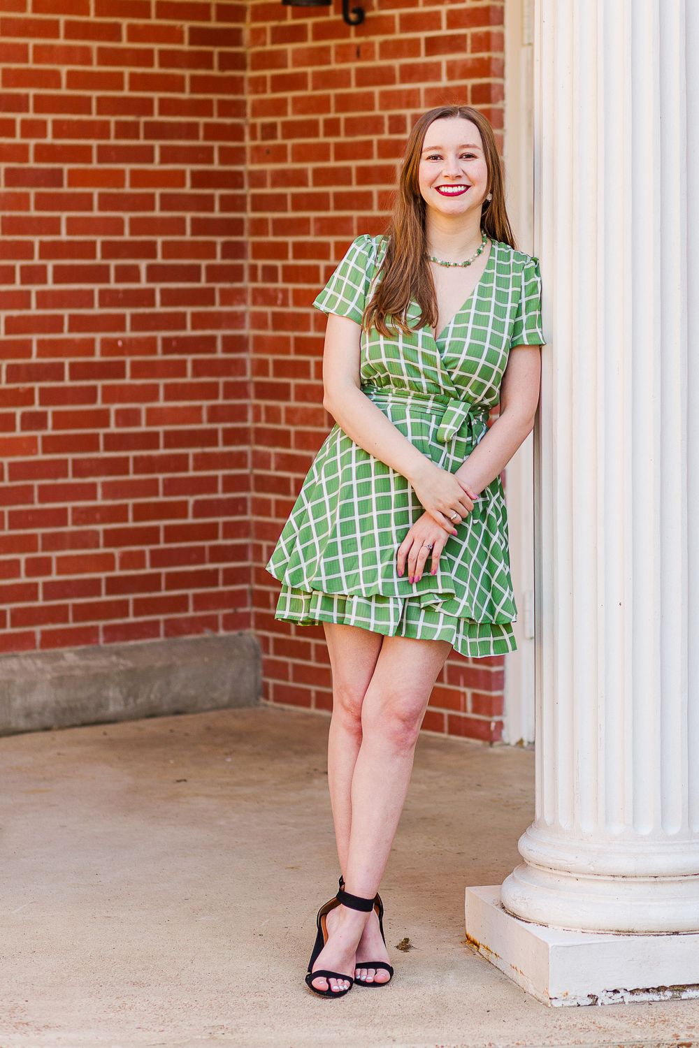 Graduate in green geometric print dress poses by white column.