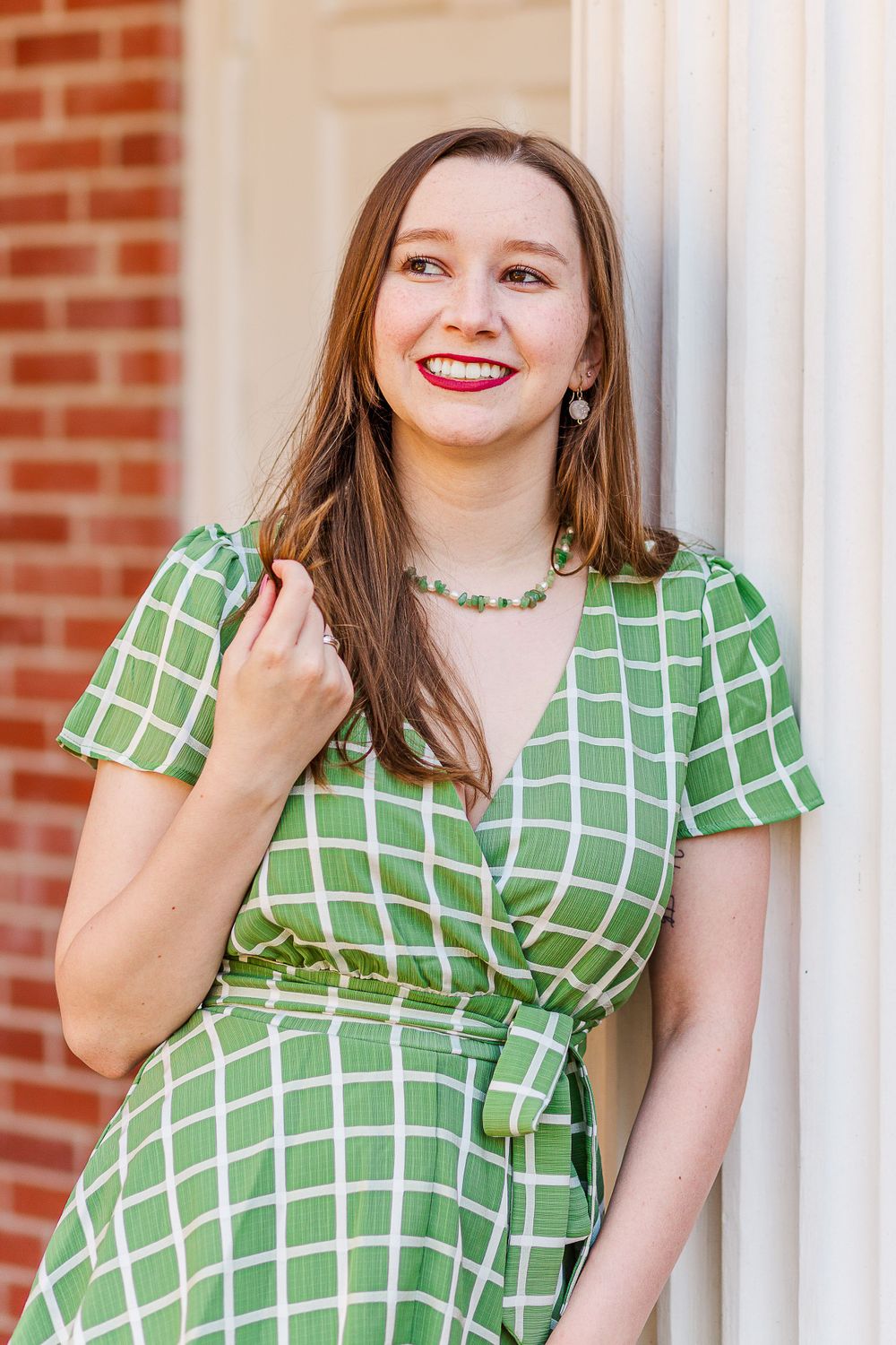 Graduate wearing green patterned wrap dress poses against white column.