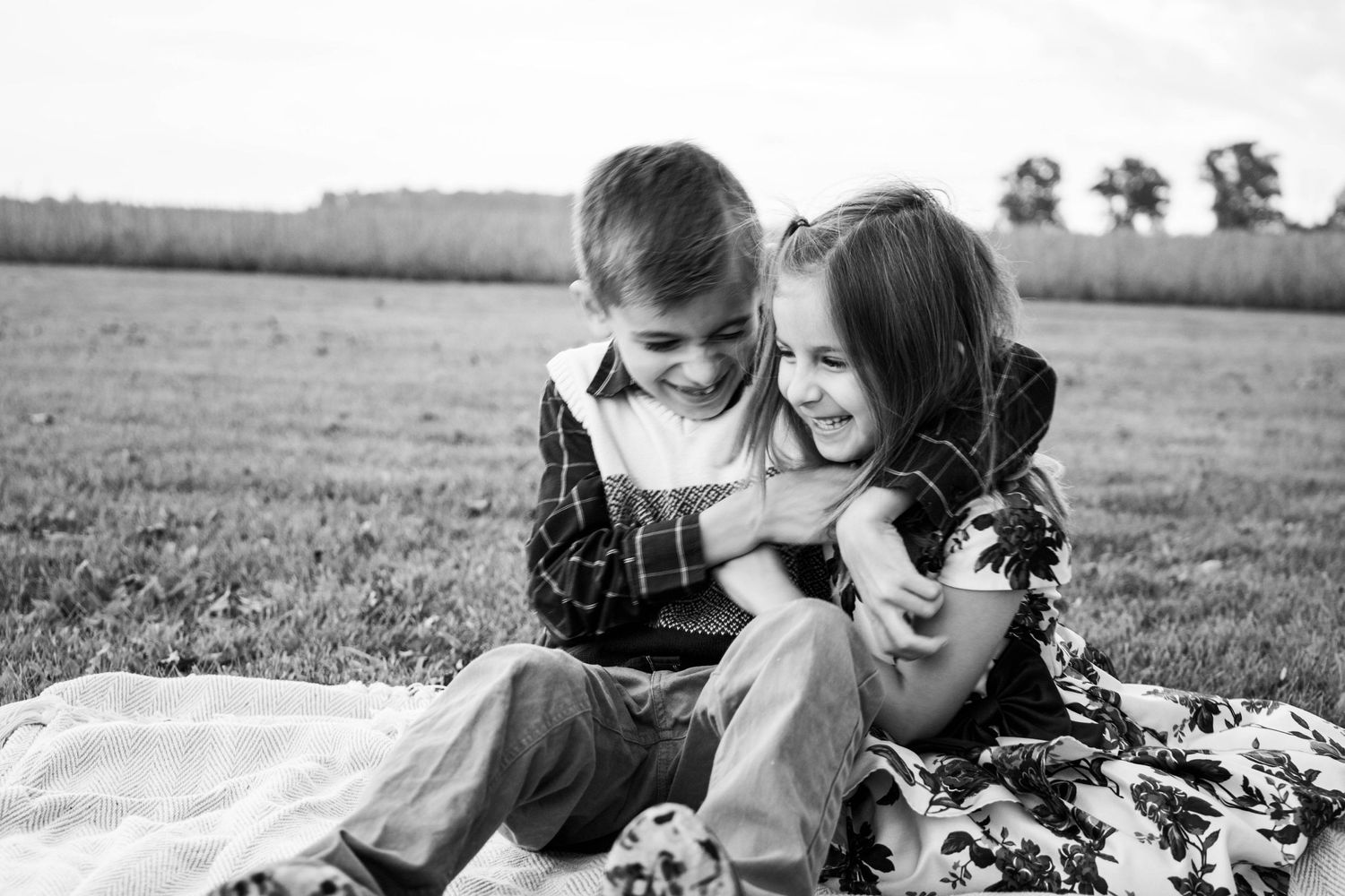 Black and white portrait of two children laughing together on a blanket outdoors.