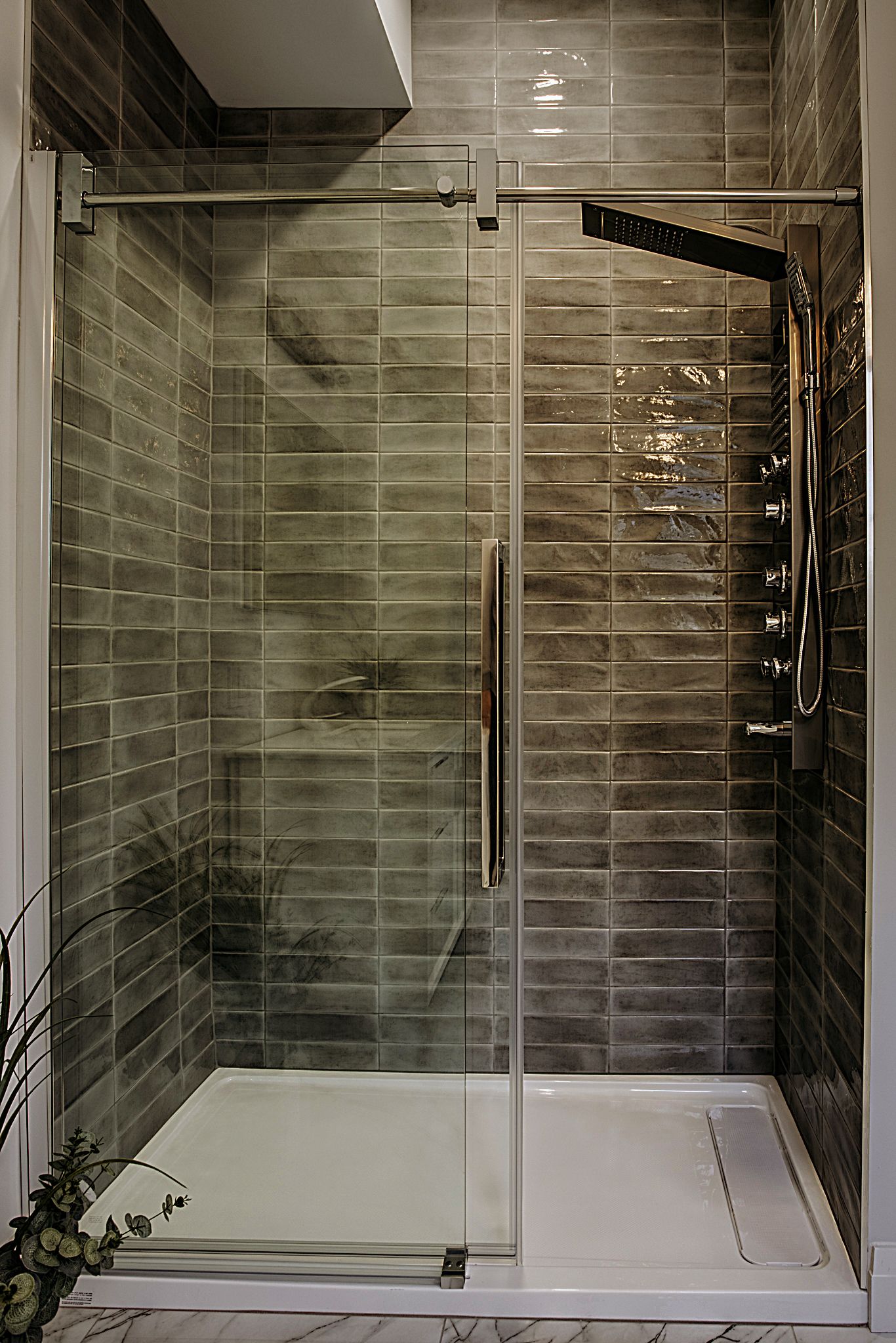 Modern bathroom interior with glass shower enclosure and gray tile walls.