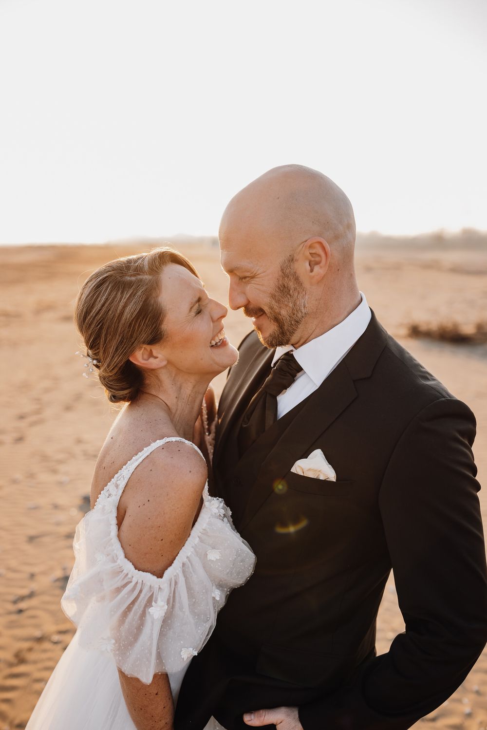Ein romantisches Hochzeitsporträt eines Paares bei Sonnenuntergang in Wüstengelände mit warmer goldener Beleuchtung.